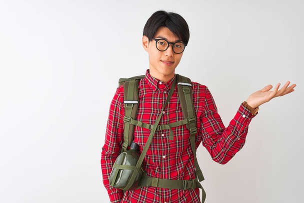 chinês caminhante homem vestindo mochila cantina óculos sobre isolado branco fundo sorrindo alegre apresentando e apontando com palma da mão olhando para a câmera
. - Foto, Imagem