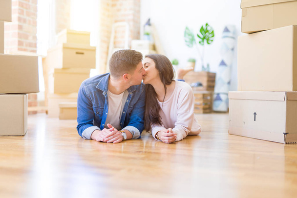 Joven hermosa pareja relajándose tumbada en el suelo alrededor de cajas de cartón en casa, sonriendo feliz de mudarse a una nueva casa
 - Foto, Imagen