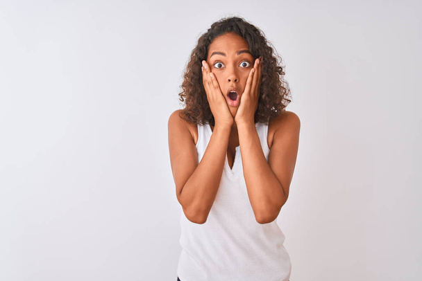 Young brazilian woman wearing casual t-shirt standing over isolated white background afraid and shocked, surprise and amazed expression with hands on face - Foto, Imagen