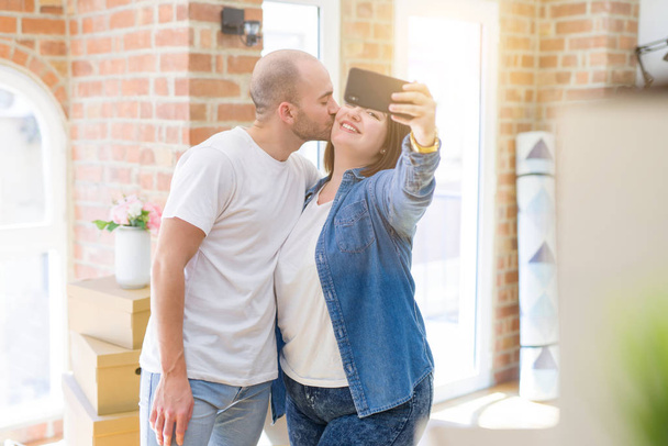 新居でスマホを使って写真を撮る若いカップル、新しいアパートに引っ越して嬉しそうに笑顔 - 写真・画像
