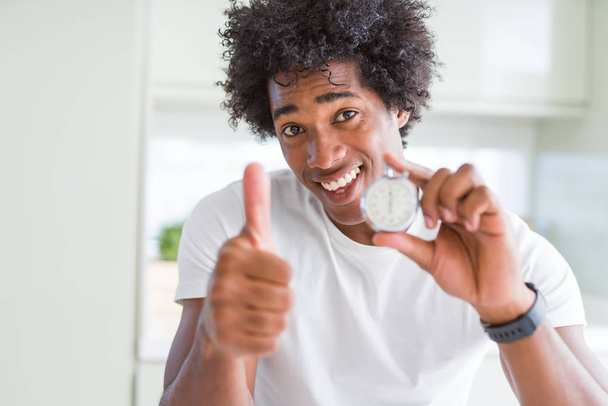 Uomo afroamericano che tiene cronometro felice con grande sorriso facendo segno ok, pollice in su con le dita, segno eccellente
 - Foto, immagini