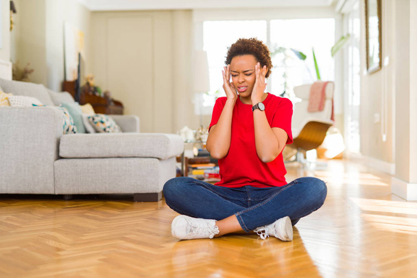 Fiatal gyönyörű afro-amerikai nő ül a padlón otthon kézzel a fejét a fájdalom a fejét, mert a stresszt. Szenvedés migrén. - Fotó, kép