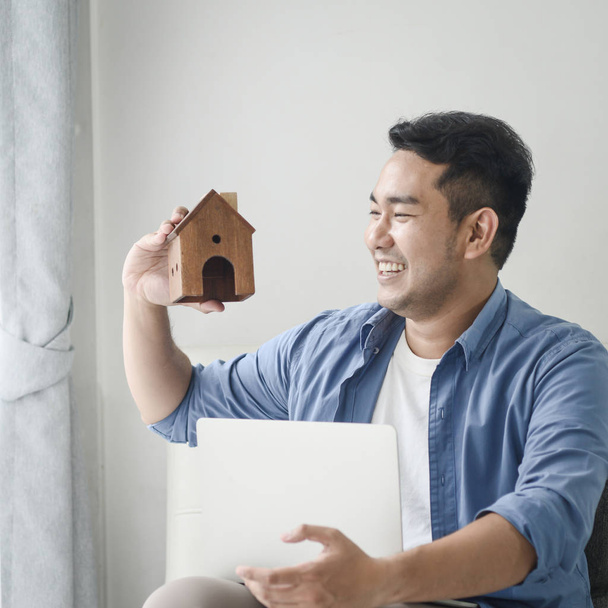 Asian man holding house in his hand and using laptop, real estat - Photo, image