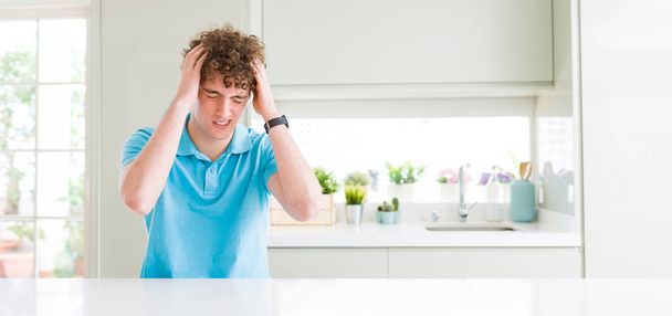 Wide shot of young handsome man at home suffering from headache desperate and stressed because pain and migraine. Hands on head. - 写真・画像