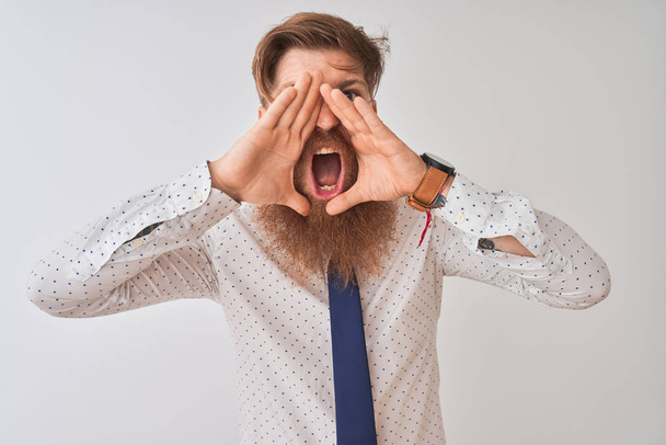 Jonge Redhead Ierse zakenman staande over geïsoleerde witte achtergrond schreeuwen boos uit luid met handen over de mond - Foto, afbeelding
