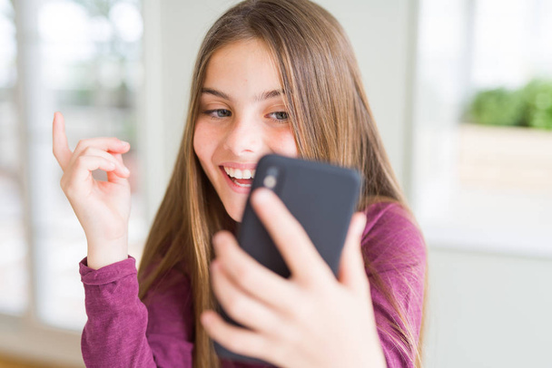 Hermosa niña enviando un mensaje usando un teléfono inteligente muy feliz apuntando con la mano y el dedo hacia un lado
 - Foto, imagen