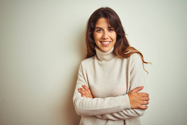 Young beautiful woman wearing winter sweater standing over white isolated background happy face smiling with crossed arms looking at the camera. Positive person. - Foto, imagen