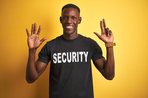 L'uomo afroamericano di salvaguardia indossa l'uniforme di sicurezza su sfondo giallo isolato mostrando e indicando con le dita il numero otto mentre sorride fiducioso e felice
. - Foto, immagini