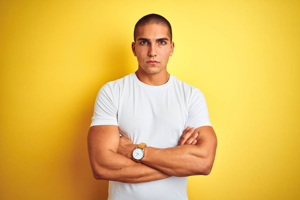Młody kaukaski mężczyzna ubrany casual biały t-shirt na żółtym białym tle sceptyczny i nerwowy, dezaprobaty wyrażenie na twarzy skrzyżowane ramiona. Osoba negatywna. - Zdjęcie, obraz