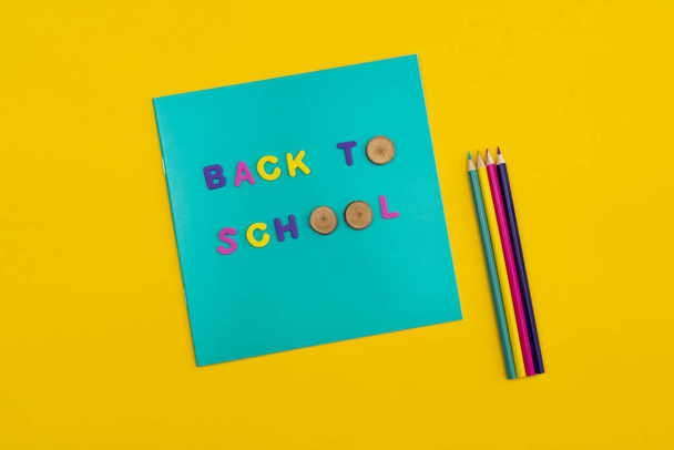 Ritorno a scuola testo su un blocco note con matite colorate accanto su sfondo giallo arancio
. - Foto, immagini