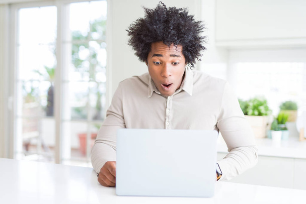 Афроамериканец, работающий с ноутбуком, напуганный от удивления лицом, напуганный и взволнованный выражением страха
 - Фото, изображение