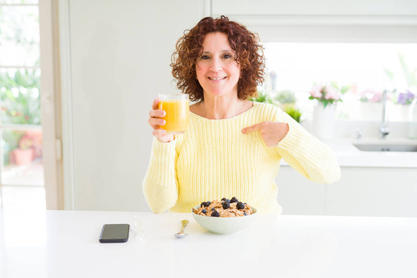 Mujer mayor comiendo desayuno saludable en la mañana en casa con la cara sorpresa señalando el dedo a sí mismo
 - Foto, imagen