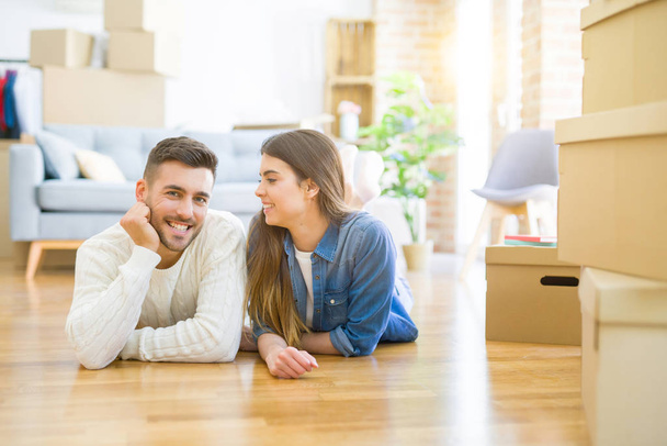 Joven hermosa pareja tumbada en el suelo de la nueva casa, sonriendo en el amor muy feliz por mudarse a un nuevo apartamento
 - Foto, imagen
