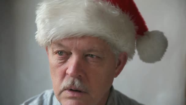 An older man in a Santa Claus hat says "ho ho ho" in a grumpy manner - Footage, Video