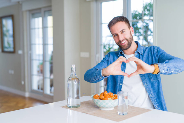 自宅でミートボールとトマトソースでパスタを食べるハンサムな男は、手でハートのシンボルと形を示す愛に微笑んでいます。ロマンチックなコンセプト. - 写真・画像