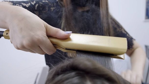 Κομμωτήριο κάνει πλαστικοποίηση και ίσιωμα των μαλλιών σε ένα σαλόνι ομορφιάς για ένα κορίτσι με καστανά μαλλιά. έννοια της φροντίδας των μαλλιών - Φωτογραφία, εικόνα