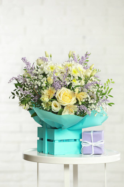 Beautiful bouquet of flowers and gift box on table against light background - Photo, Image