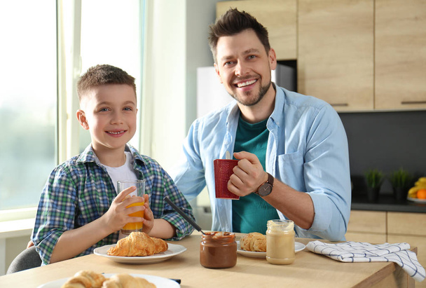 Dad and son having breakfast together in kitchen - Fotó, kép