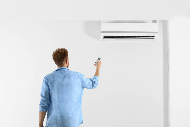 Young man operating air conditioner with remote control indoors. Space for text - Photo, Image