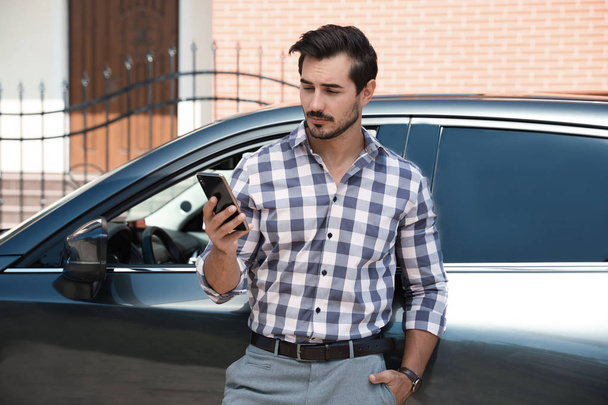 attraktiver junger Mann mit Smartphone in der Nähe von Luxusauto - Foto, Bild