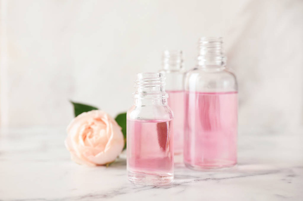 Bottles of essential oil and rose on marble table - Фото, изображение
