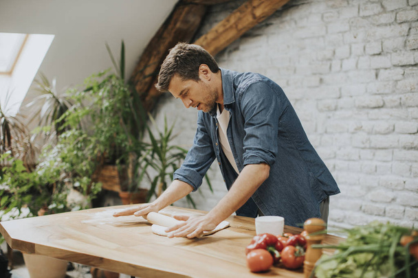 Csinos fiatal férfi készít tésztát házi kenyér a konyhában - Fotó, kép