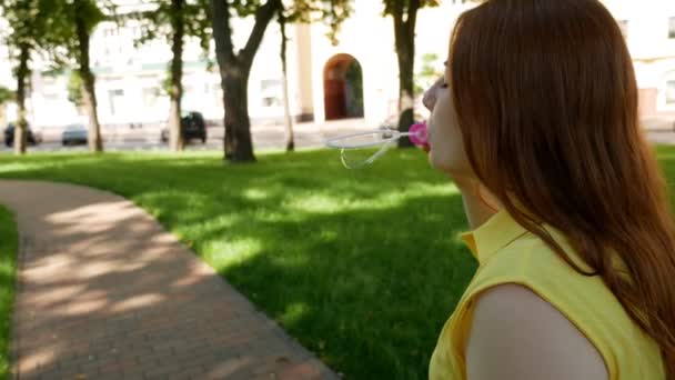 Red-haired girl blows soap bubbles in the park.yellow dress She smiling and laughing.summer and happiness  - Footage, Video