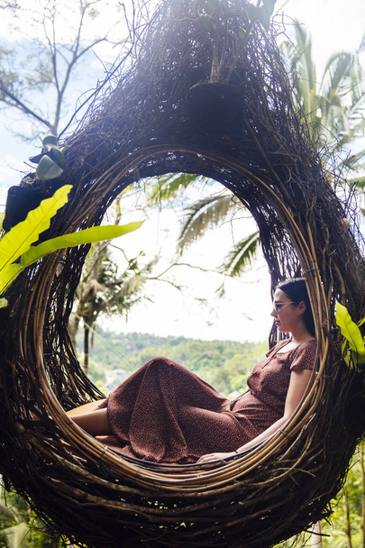 A female tourist is sitting on a large bird nest on a tree at Bali island, Indonesia - Photo, Image
