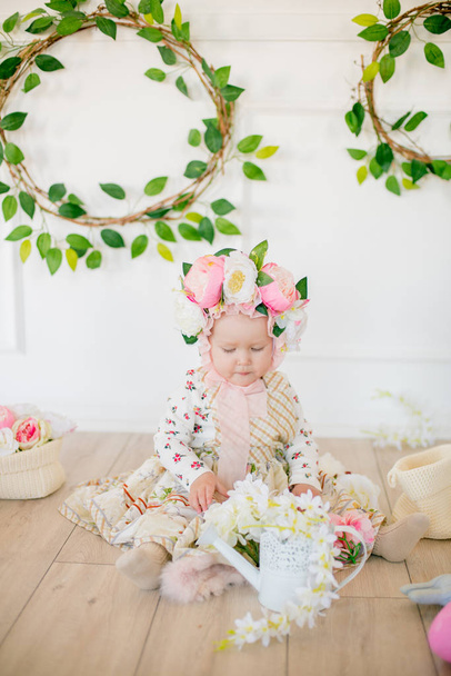 Linda niña en un vestido con un estampado de flores y un sombrero con flores en la decoración de Pascua en el estudio. Niña con huevos de Pascua y flores en un estudio de primavera
 - Foto, imagen