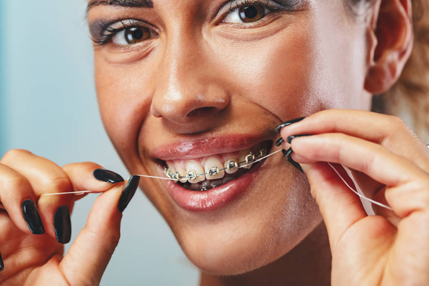 歯をフロッシングするブレースを持つ笑顔の女性の顔のクローズアップ - 写真・画像