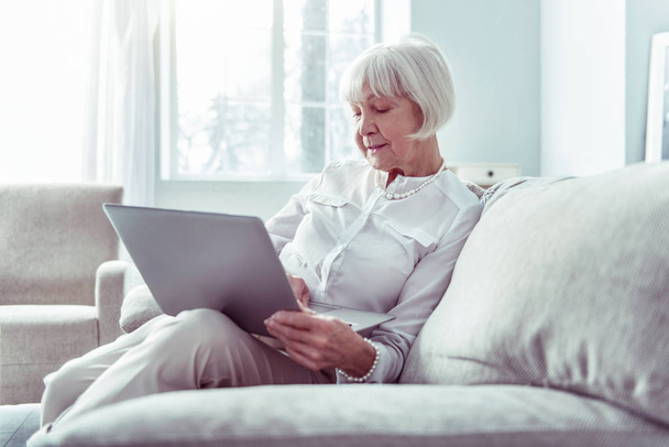 Modern retired woman holding silver laptop while watching video - Valokuva, kuva