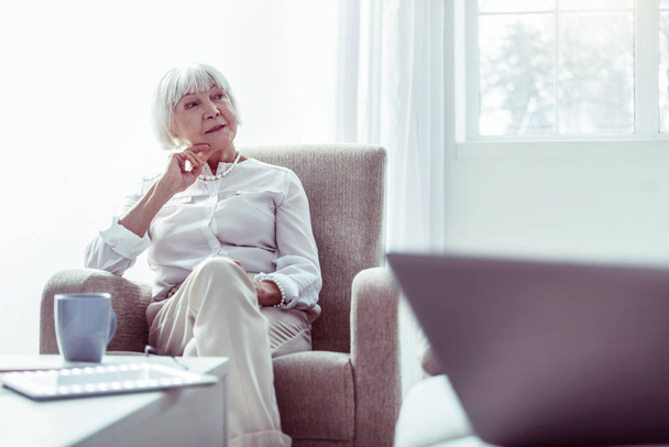Elegant retired woman sitting in armchair standing near the window - Photo, Image