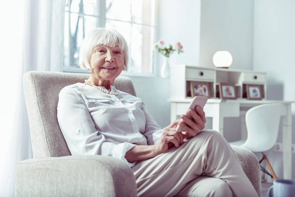 Pleasant beaming senior lady holding her pink smartphone calling daughter - Photo, Image
