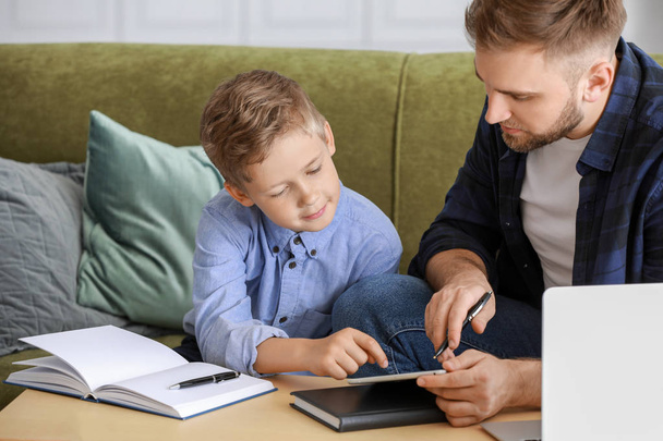 Ο πατέρας βοηθάει το γιο του να κάνει μαθήματα στο σπίτι. - Φωτογραφία, εικόνα