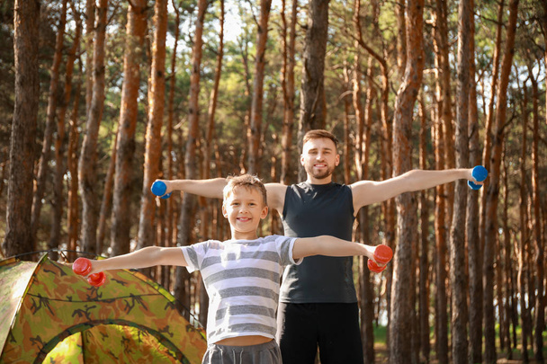Father and his little son training with dumbbells near camping tent in forest - 写真・画像