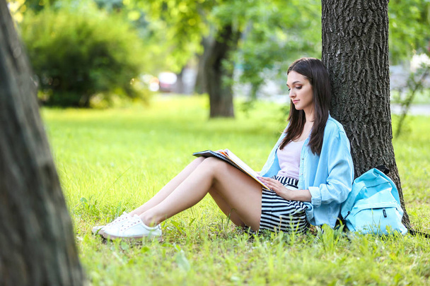 Estudante bonita sentada debaixo da árvore no parque
 - Foto, Imagem