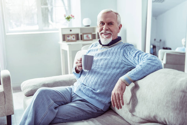 Σύγχρονος συνταξιούχος άνθρωπος έχει κάποια ξεκούραση στο σπίτι πίνοντας φλιτζάνι τσαγιού - Φωτογραφία, εικόνα