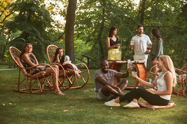 glückliche Freunde beim Essen und Trinken von Bier beim Barbecue-Dinner bei Sonnenuntergang - Foto, Bild
