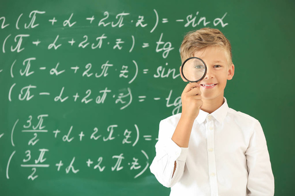 Little boy with magnifying glass near school blackboard in classroom - Photo, Image