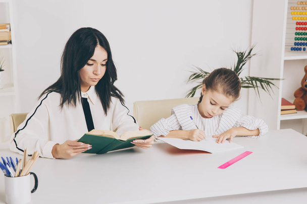 Мать и дочь читают. Учимся вместе, сидя за столом
. - Фото, изображение