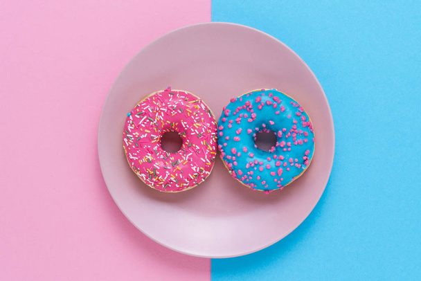 Γλυκά και πολύχρωμα ντόνατς στο πιάτο σε ροζ-μπλε φόντο. Κορυφαία προβολή, Χώρος αντιγραφής. - Φωτογραφία, εικόνα
