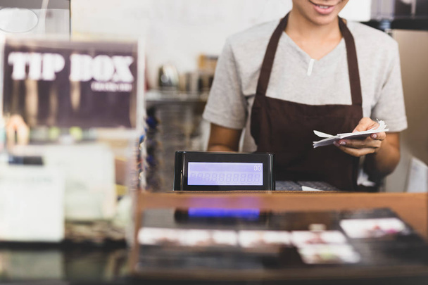 Female cashier operating cash register with order in her hand in cafe. - Photo, Image