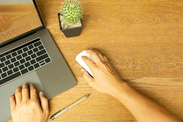 Widok z góry na rękę człowieka biznesu za pomocą laptopa i trzymając mysz z długopisem na drewnianym biurku. - Zdjęcie, obraz