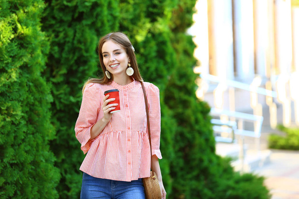 Stylish young woman with cup of coffee outdoors - Fotó, kép