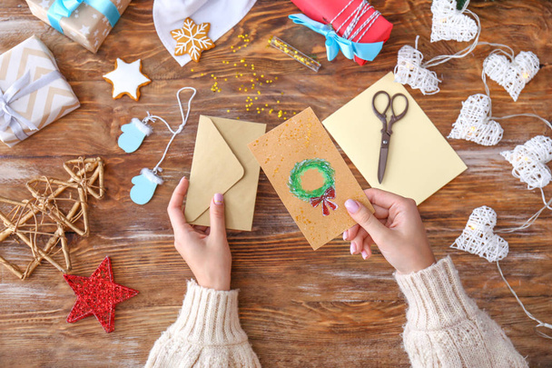 Жінка з конвертом і різдвяною листівкою ручної роботи за дерев'яним столом
 - Фото, зображення
