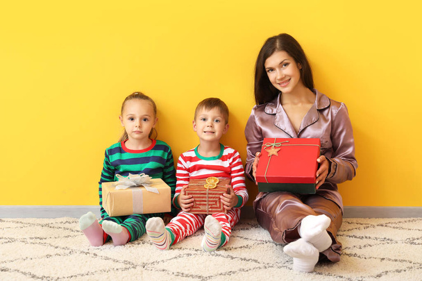 Mujer y sus pequeños hijos con regalos de Navidad sentados cerca de la pared de color
 - Foto, imagen
