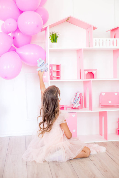Cute happy girl in a beautiful dress at home plays with a dollhouse and toys - Foto, imagen