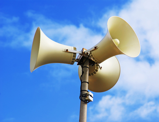 Drie luidsprekers bevestigd aan een mast tegen een achtergrond van blauwe lucht.                    - Foto, afbeelding