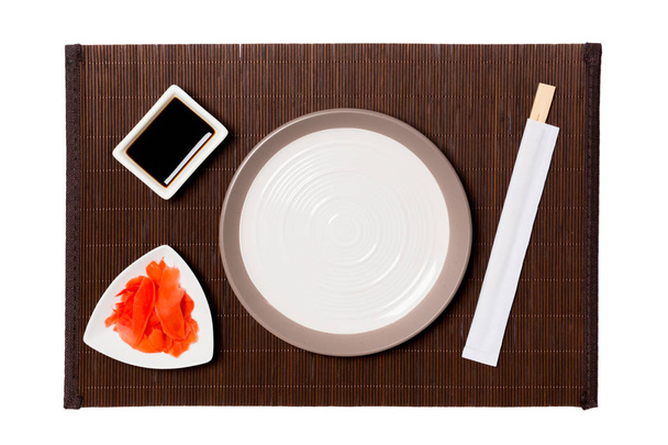 Üres kerek fehér lemez pálcika a sushi, gyömbér és szójaszósz a sötét bambusz szőnyeg háttérben. Felülnézet másolási területtel a tervezéshez - Fotó, kép