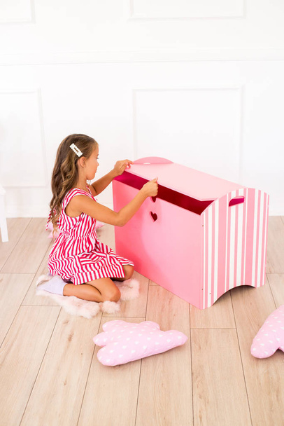 Cute girl in a beautiful dress at home plays with a decorative chest and toys - Photo, image